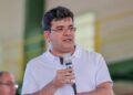 Rafael Fonteles, governador do Piauí desde 2023 , de camisa polo branca e óculos, segura microfone durante discurso em ginásio
