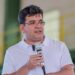 Rafael Fonteles, governador do Piauí desde 2023 , de camisa polo branca e óculos, segura microfone durante discurso em ginásio
