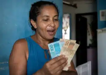 Mulher segurando cédulas de dinheiro e conferindo valor, representando o novo lote do auxílio de R$ 7,3 mil liberado pelo governo.