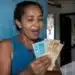 Mulher segurando cédulas de dinheiro e conferindo valor, representando o novo lote do auxílio de R$ 7,3 mil liberado pelo governo.