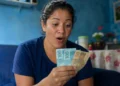 Mulher segurando notas de dinheiro representando o depósito de novo lote do auxílio de R$ 7.300 pela CAIXA.