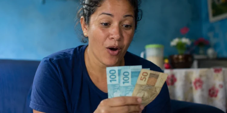 Mulher segurando notas de dinheiro representando o depósito de novo lote do auxílio de R$ 7.300 pela CAIXA.
