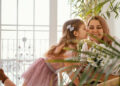 Menina beijando a mãe no rosto enquanto entrega um buquê de flores brancas