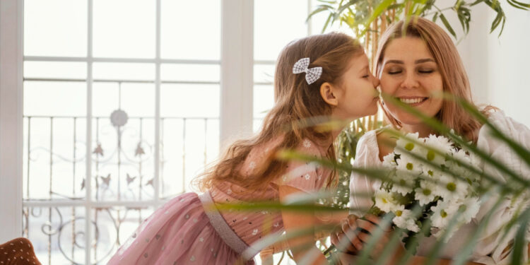 Menina beijando a mãe no rosto enquanto entrega um buquê de flores brancas