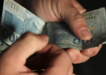 Mãos contando cédulas de cem reais durante recebimento do Bolsa Família