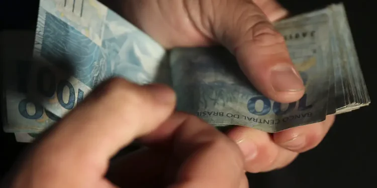 Mãos contando cédulas de cem reais durante recebimento do Bolsa Família