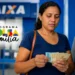Mulher conferindo notas de dinheiro em caixa eletrônico da Caixa, representando beneficiários do Bolsa Família com NIS final 3 que recebem pagamento de R$ 850 nesta quarta-feira (20).
