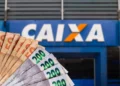 Cédulas de real em frente a agência da CAIXA representando o pagamento de R$ 7,3 mil para famílias beneficiadas