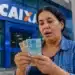 Mulher conferindo notas de R$ 50 e R$ 100 em frente a uma agência da Caixa, representando o pagamento de R$ 1.128,01.