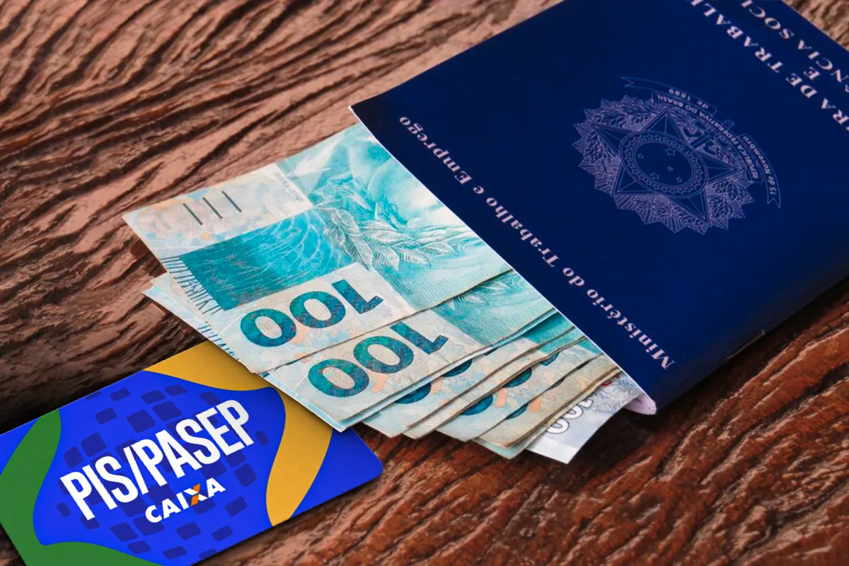 Carteira de Trabalho azul com cédulas de cem reais ao lado de cartão do PIS Pasep da Caixa sobre mesa de madeira