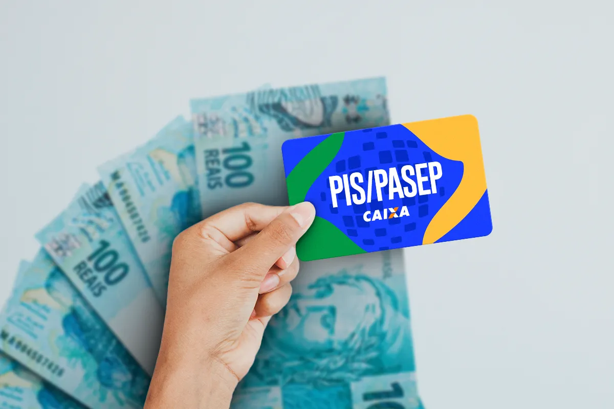 Mão segurando cartão PIS/PASEP com logo da Caixa, cores verde, azul e amarelo, com notas de R$ 100 ao fundo