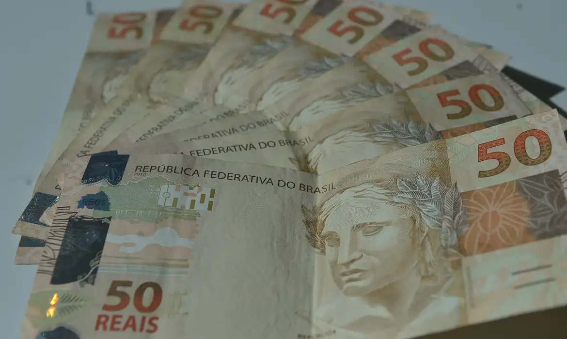 Várias notas de cinquenta reais dispostas em formato de leque sobre superfície clara