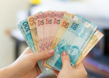 Mãos seguram em leque cédulas de dez, cinquenta e cem reais.