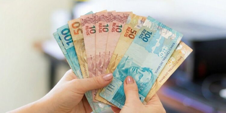 Mãos seguram em leque cédulas de dez, cinquenta e cem reais.