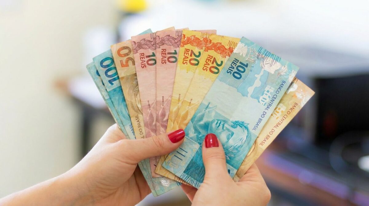 Mãos seguram em leque cédulas de dez, vinte, cinquenta e cem reais.