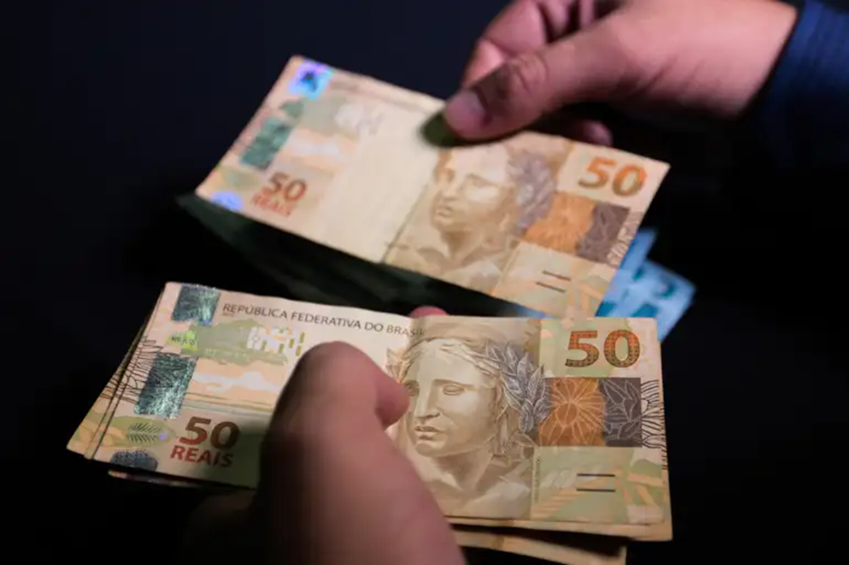 Mãos manuseando notas de cinquenta reais durante recebimento do teto previdenciário do INSS