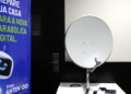 Kit da nova parabólica digital exposto ao lado do banner da campanha Siga Antenado da Anatel sobre a troca de antenas