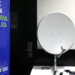 Kit da nova parabólica digital exposto ao lado do banner da campanha Siga Antenado da Anatel sobre a troca de antenas