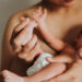 Mãe segura o bebê recém-nascido nos braços, com a mãozinha da criança apoiada em sua mão.