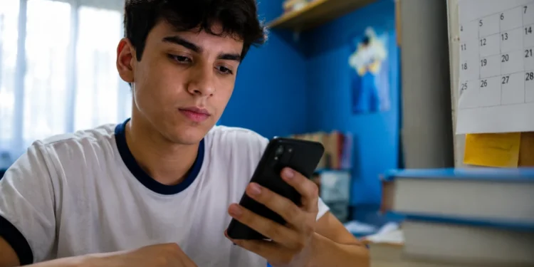 Estudante consulta o celular enquanto estuda, representando a busca de informações sobre o valor e o prazo de pagamento da taxa do Enem 2026.