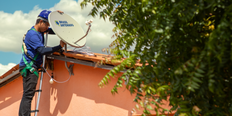 Técnico instala antena parabólica digital Brasil Antenado no telhado de casa residencial
