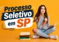 Estudante de cabelo castanho segura lápis enquanto pensa, com caderno aberto, pilha de livros e fundo amarelo
