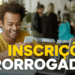 Jovem negro sorridente de cabelo crespo e camiseta amarela olha celular em cafeteria com notebook aberto