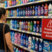 Consumidora observa prateleira de supermercado com produtos Ypê e placa vermelha de alerta "Produtos suspensos Anvisa"