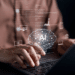 Mãos digitando em laptop com holograma de cérebro AI e ícones de tecnologia flutuando sobre teclado.