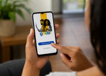 Mulher segura celular com tela do app gov.br e toca botão "Entrar com gov.br" em ambiente interno.