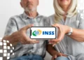 Casal idoso segura celular horizontal mostrando logo do INSS nas cores verde, amarelo e azul, em ambiente claro
