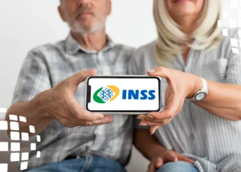 Casal idoso segura celular horizontal mostrando logo do INSS nas cores verde, amarelo e azul, em ambiente claro