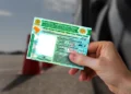Pessoa segurando uma CNH em frente a um veículo, representando regras de renovação automática da carteira de motorista.