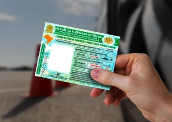 Pessoa segurando uma CNH em frente a um veículo, representando regras de renovação automática da carteira de motorista.