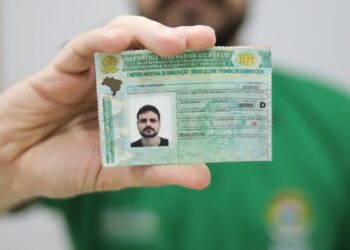 Homem exibindo a Carteira Nacional de Habilitação brasileira em destaque para a câmera