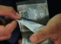 Mãos contando notas de cem reais durante recebimento de valores do abono salarial PIS/Pasep