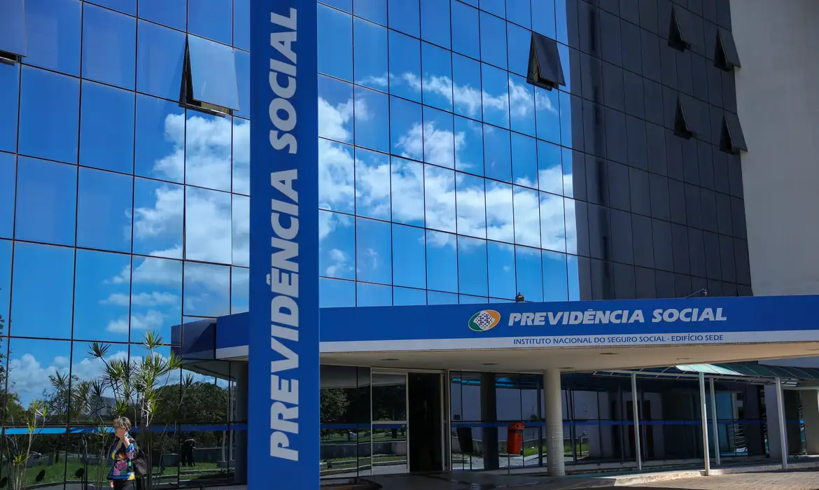 Fachada espelhada do edifício sede do INSS com letreiro azul "Previdência Social" e céu refletido nos vidros