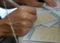 Mãos preenchendo volante da Mega-Sena com caneta sobre mesa em casa lotérica