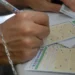 Mãos preenchendo volante da Mega-Sena com caneta sobre mesa em casa lotérica