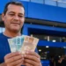 Homem segurando notas de reais em frente a uma agência bancária representando a liberação de saque-aniversário do FGTS em maio