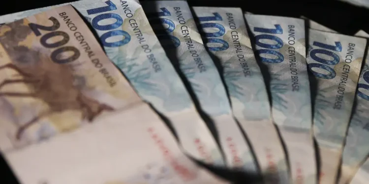 Leque de cédulas de duzentos e cem reais espalhadas sobre superfície escura em close com iluminação lateral