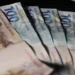 Leque de cédulas de duzentos e cem reais espalhadas sobre superfície escura em close com iluminação lateral