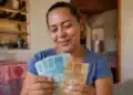 Mulher brasileira segura notas de real dentro de casa, representando o saque do Bolsa Família de maio para beneficiários com NIS final 9.