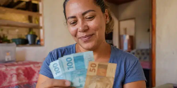 Mulher brasileira segura notas de real dentro de casa, representando o saque do Bolsa Família de maio para beneficiários com NIS final 9.
