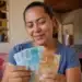 Mulher brasileira segura notas de real dentro de casa, representando o saque do Bolsa Família de maio para beneficiários com NIS final 9.