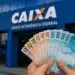 Saque de notas de real em frente à agência da Caixa Econômica Federal, relacionado à liberação de R$ 6.220 para novos brasileiros.