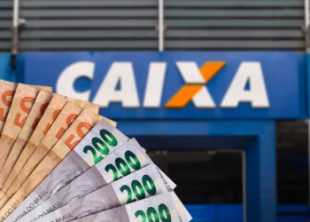 Notas de reais em frente a uma agência da Caixa, representando saque de R$ 6.220 disponível para solicitação.