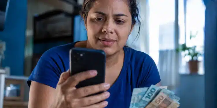 Mulher consulta no celular informações sobre o saque de R$ 6.220 da Caixa, representando a solicitação do valor, que pode ser feita até 30 de maio.