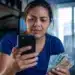 Mulher consulta no celular informações sobre o saque de R$ 6.220 da Caixa, representando a solicitação do valor, que pode ser feita até 30 de maio.