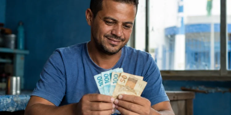 Homem segurando cédulas em ambiente doméstico, ilustrando o saque do FGTS de R$ 6.220 liberado para solicitação a partir de 27 de maio.